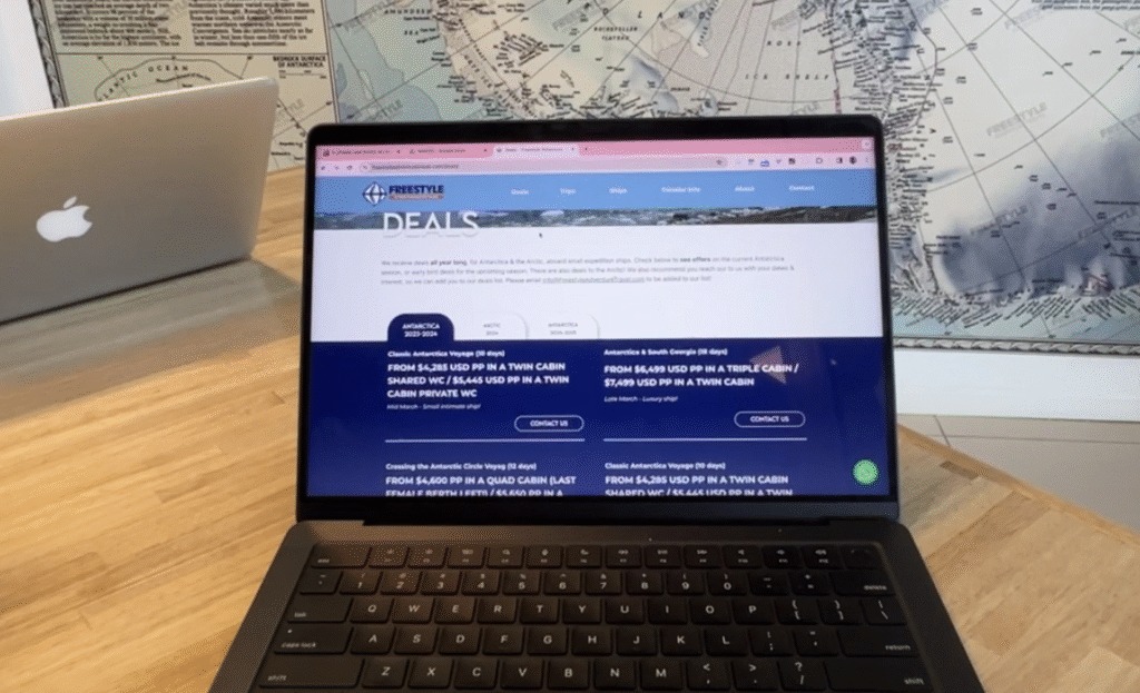 Laptop displaying Antarctica travel deals on Freestyle Adventure Travel site, with Antarctic map and MacBook in the background